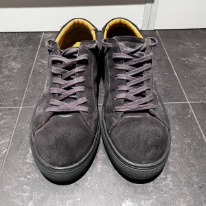 Svarta mocka sneakers (myrqvist) - Säljer ett par snygga svarta sneakers i mocka. De har en klassisk design med snörning och en bekväm passform. Insidan är fodrad i en kontrasterande gul färg som ger en cool touch. Perfekta för både vardag och fest!