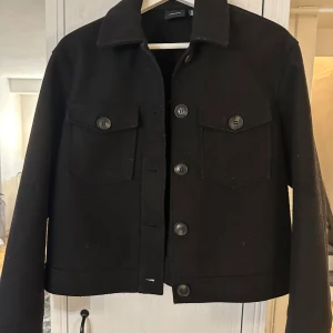 Svart kappa med knappar - Säljer en stilren svart kappa i mycket bra skick. Perfekt för höst och vår, och funkar både till vardags och fest. Köpt förra året men fortfarande i bra skick! 