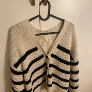 Randig kofta från H&M - Säljer en superfin randig kofta från H&M i storlek L. Den är vit med svarta ränder och har en skön, stickad känsla. Perfekt för höst och vår! Koftan har en v-ringad design och knappar framtill. Passar både till vardags och lite finare tillfällen.