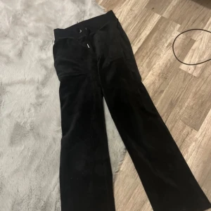 Svarta byxor från Juicy Couture - Säljer ett par svarta byxor från Juicy Couture i storlek XXS. De är i mjukt material och har en broderad logga på framsidan. Byxorna har en klassisk stil med fickor bak och knappar. Perfekta för en avslappnad men stilren look!
