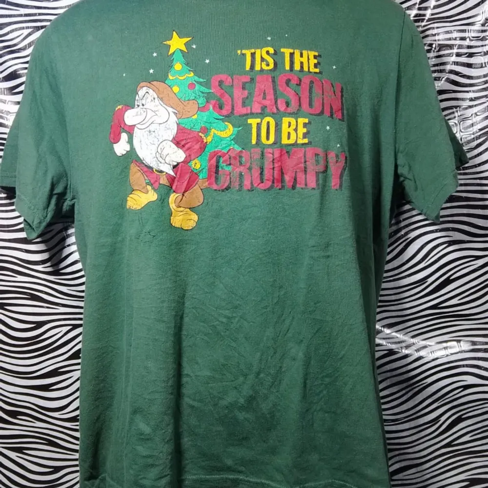 Säljer en grön t-shirt med ett roligt jultryck. Texten 'Tis the season to be grumpy' och en tecknad figur i tomtedräkt gör den perfekt för julens alla fester. Tröjan är kortärmad och i bomull, vilket gör den bekväm att bära hela dagen. Perfekt för dig som vill sprida lite humor under julen! 🎄. T-shirts.