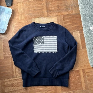 North Sails stickad tröja - Säljer en snygg mörkblå tröja med ett coolt flaggmönster på bröstet. Perfekt för höst och vinter med sin varma och sköna känsla. Tröjan har långa ärmar och ribbade muddar vid ärmslut och nederkant. Passar både till vardags och fest!