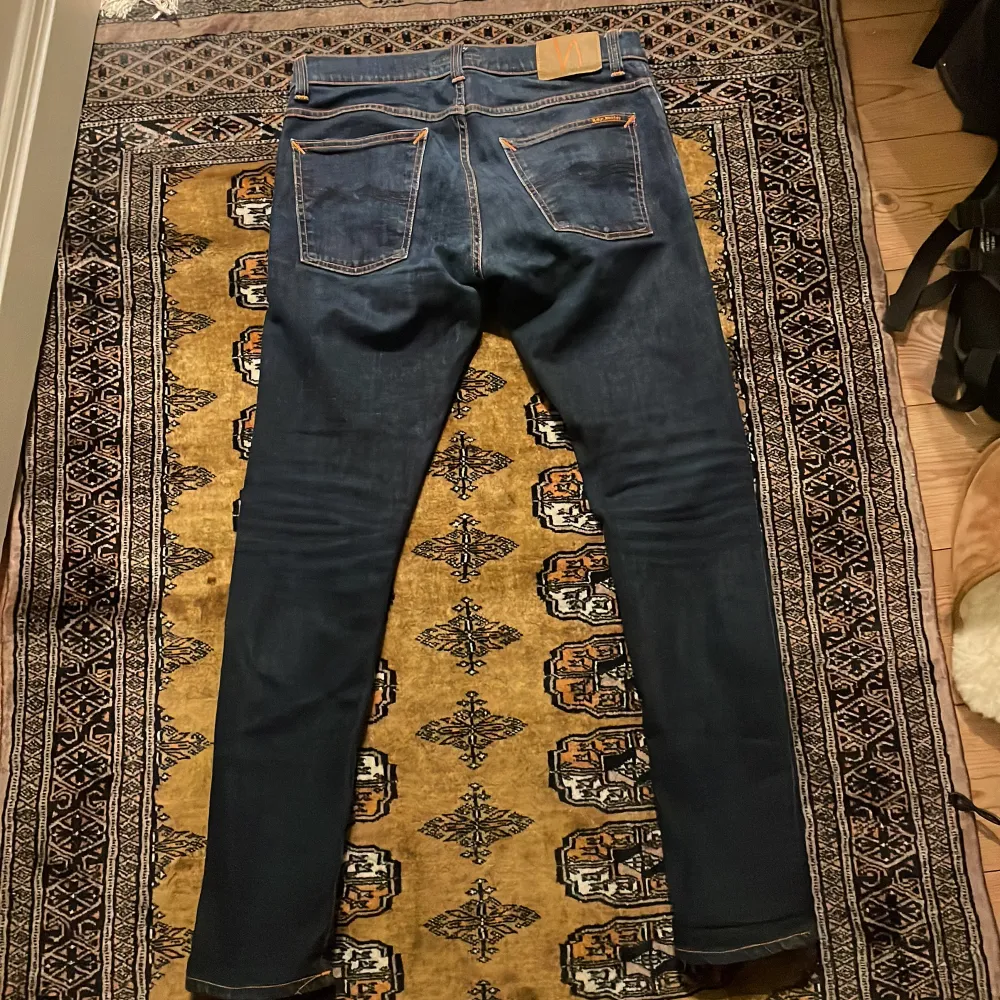 Säljer ett par mörkblå jeans från Nudie i bra skick. De har en slim passform och är tillverkade i denim med klassiska orange sömmar. Perfekta för både vardag och fest! 🕺. Jeans & Byxor.