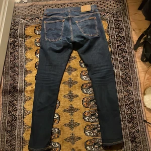  Nudie Jeans - Säljer ett par mörkblå jeans från Nudie i bra skick. De har en slim passform och är tillverkade i denim med klassiska orange sömmar. Perfekta för både vardag och fest! 🕺