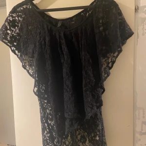 Svart spetsblus - Säljer en elegant svart spetsblus med korta ärmar och volangdetaljer. Perfekt för en festlig kväll eller en utekväll med vänner. Blusen har en luftig passform och är i mycket bra skick.