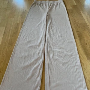 Beige ribbade byxor från Bik Bok - Säljer ett par superbekväma beige ribbade byxor från Bik Bok i storlek L. De har en loose passform och är perfekta för både vardag och hemmakvällar. 