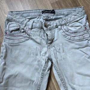 Grå low waist lågmidjade jeans från Detroit - Säljer ett par grå jeans från Detroit i bra skick. De har snygga röda sömmar och nitar på fickorna. Det finns en liten fläck på framsidan och baksidan (se bild), men annars är de i fint skick. 