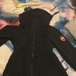 Svart jacka från Canada Goose köpt för 13 tusen jätte fin jacka. Passar som S M och L väldig skön i materialet men inte så tjock  - Säljer en svart jacka från Canada Goose i mycket bra skick. Jackan har en huva och långa ärmar, perfekt för kalla vinterdagar. Den är gjord av slitstarkt material och har en dragkedja framtill. Passar både till vardags och mer äventyrliga aktiviteter.