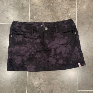 Svart batikmönstrad kortkjol - Säljer en cool unik svart kortkjol från Addict med batikmönster. Kjolen har fina detaljer.