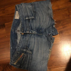 Blå lågmidjade jeansshorts från Diesel - Säljer ett par snygga blå jeansshorts från Diesel i bra skick. De har en cool slitning och fransiga kanter för en avslappnad look. Perfekta för sommardagar eller festivaler! 💋💋