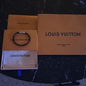 Svart armband från Louis Vuitton - Säljer ett stilrent svart armband från Louis Vuitton. Armbandet har en elegant design med en metallisk låsdetalj som ger en lyxig känsla. Perfekt accessoar för både vardag och fest. Kommer med originalförpackning och påse.