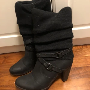 Svarta boots med stickad detalj och klack - Snygga svarta boots från Super Me med en cool stickad överdel och dekorativa remmar med nitar. De har en bekväm klack och spetsig tå, perfekt för höst och vinter. Dragkedja på sidan för enkel på- och avtagning. Passar både till vardags och fest!