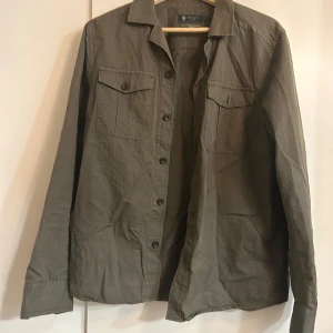 Olivgrön skjorta från Riley - Säljer en olivgrön skjorta från Riley i slim fit. Skjortan har långa ärmar och knappar framtill samt två bröstfickor med knappar. Perfekt för både vardag och fest! 🕺