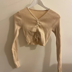 Beige ribbad topp - Säljer en superfin beige ribbad topp med lång ärm och v-ringning. Den har en snygg knytning framtill som ger en cool look 🧡