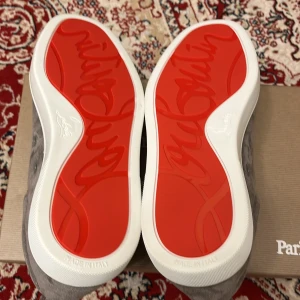 Grå sneakers från Christian Louboutin - Säljer ett par snygga grå sneakers från Christian Louboutin i mocka. De har den ikoniska röda sulan och är i mycket bra skick. Perfekta för både vardag och fest! Skorna har snörning och en stilren design som passar till det mesta.