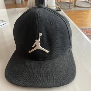 Svart keps med broderad logga - Säljer en svart keps från Jordan med den ikoniska broderade loggan framtill. Kepsen har en klassisk design med böjd skärm och justerbar passform. Perfekt för både vardag och sportiga aktiviteter. Kvalitet inspirerad av den största spelaren någonsin! Skriv för frågor ☝️