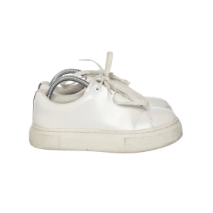 Eytys Vita sneakers med lila detalj - Säljer ett par vita sneakers i bra skick med en cool lila rand på hälen. De har snörning och en chunky sula som ger extra komfort. Perfekta för vardagsbruk och passar till nästan allt i garderoben. Skorna är stilrena och lätta att matcha med olika outfits.