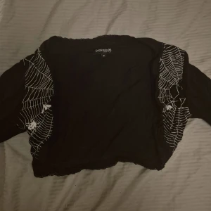 Svart bolerotopp med spindelnätsmönster från Gothicana - Säljer en cool svart bolerotopp från Gothicana med ett unikt spindelnätsmönster och små spindlar på ärmarna. Perfekt för en edgy look eller Halloween-fest! Toppen är i bra skick och har en tight passform. 🕸️🖤