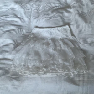 Vit volangkjol - Säljer en superfin vit kortkjol med volanger. Perfekt för sommardagar eller festliga tillfällen typ som julafton eller ny år.Kjolen har ett elastiskt midjeband för en bekväm passform. Den är lätt och luftig, vilket gör den idealisk för varma dagar. Passar perfekt med en söt topp eller blus!🥰