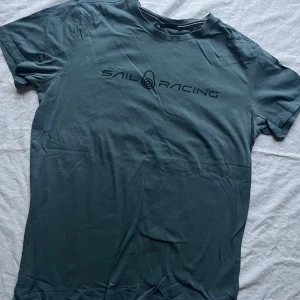 Grå t-shirt från Sail Racing - Säljer en grå t-shirt från Sail Racing i storlek M. Den är kortärmad och har en stilren logga på bröstet. Perfekt för vardagsbruk eller en avslappnad dag ute. Materialet känns mjukt och bekvämt.