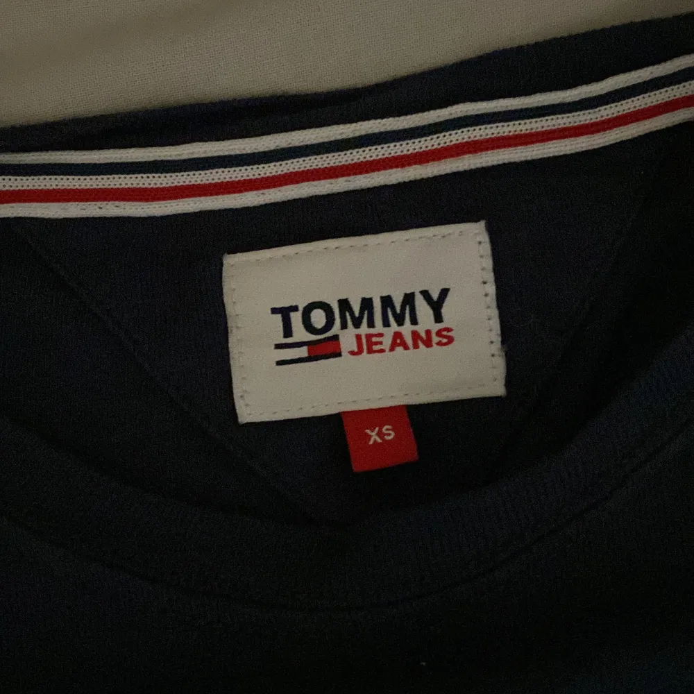 Säljer en snygg mörkblå långärmad tröja från Tommy Jeans i storlek XS. Perfekt för både vardag och lite finare tillfällen. Den är i bra skick och har en liten logga på bröstet. Passar perfekt till jeans eller chinos!. Tröjor & Koftor.