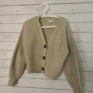 Beige ribbad kofta - Säljer en superfin beige kofta från hm med ribbad struktur och stora knappar framtill. Den har en v-ringad design och långa ärmar. Koftan är i bra skick då den knappast är använd! 