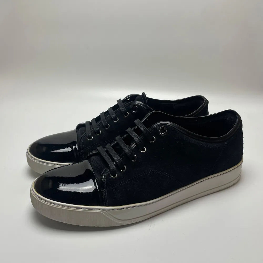 Säljer ett par stilrena mörkblåa sneakers från Lanvin i bra skick. Skorna har en blank tå och snörning, vilket ger dem en elegant touch. Perfekta för både vardag och fest! Sulan är vit och har lite slitage, men inget som påverkar användningen. Passar perfekt till jeans eller en mer uppklädd stil. Uk 10 passar 45. Skor.