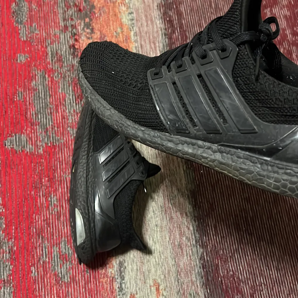 Säljer ett par svarta Adidas Ultraboost i bra skick. De har en snygg och stilren design med den klassiska tre-randiga loggan på sidan. Skorna är gjorda i ett bekvämt och flexibelt material som passar perfekt för träning eller vardagsbruk. Sulan är i bra skick och ger bra dämpning.. Skor.