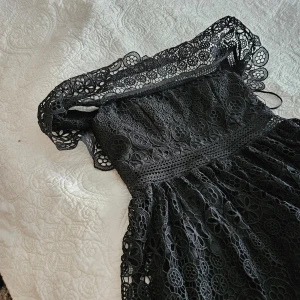 Svart spetsklänning från By malina  - Säljer en elegant svart klänning från By malina i storlek M. Klänningen har ett vackert spetsmönster och en dragkedja i sidan. Perfekt för festliga tillfällen med sin stilrena design och detaljerade spets.