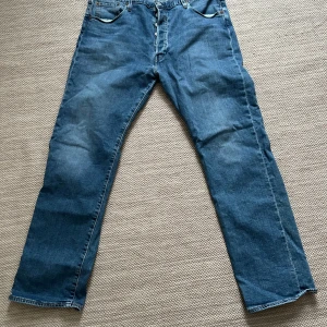 Levi's 501 Jeans - Säljer ett par klassiska Levi's 501 jeans i blå denim. W38/L32 de har en straight passform och är i bra skick. Tillverkade av 94% bomull och 6% polyester, vilket ger en skön och hållbar känsla. Perfekta för både vardag och fest!
