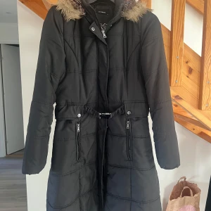 Svart lång vinterjacka med fuskpäls - Säljer en svart lång vinterjacka från Esprit i mycket bra skick. Jackan har en mysig fuskpäls vid huvan och praktiska dragkedjor framtill. Perfekt för kalla vinterdagar! ❄️