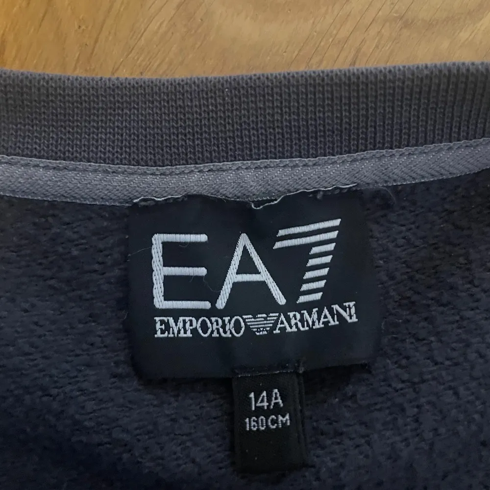 Säljer en grå sweatshirt från Emporio Armani EA7. Tröjan har en klassisk rund halsringning och långa ärmar med EA7-logga på ärmarna. Perfekt för en casual look eller träning. Den är i mycket bra skick. Fläcken i mitten är bara en lite som kan tvättas bor med vatten om jag ska fixa!. Tröjor & Koftor.