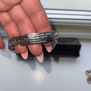 Silverfärgat armband med gravyr - Säljer ett stilrent silverfärgat armband med en platta som har gravyr. Armbandet har en klassisk kedjedesign och är perfekt för både vardag och fest. Det är i mycket bra skick och passar de flesta handleder. Perfekt som en personlig present eller för att komplettera din egen smyckessamling.