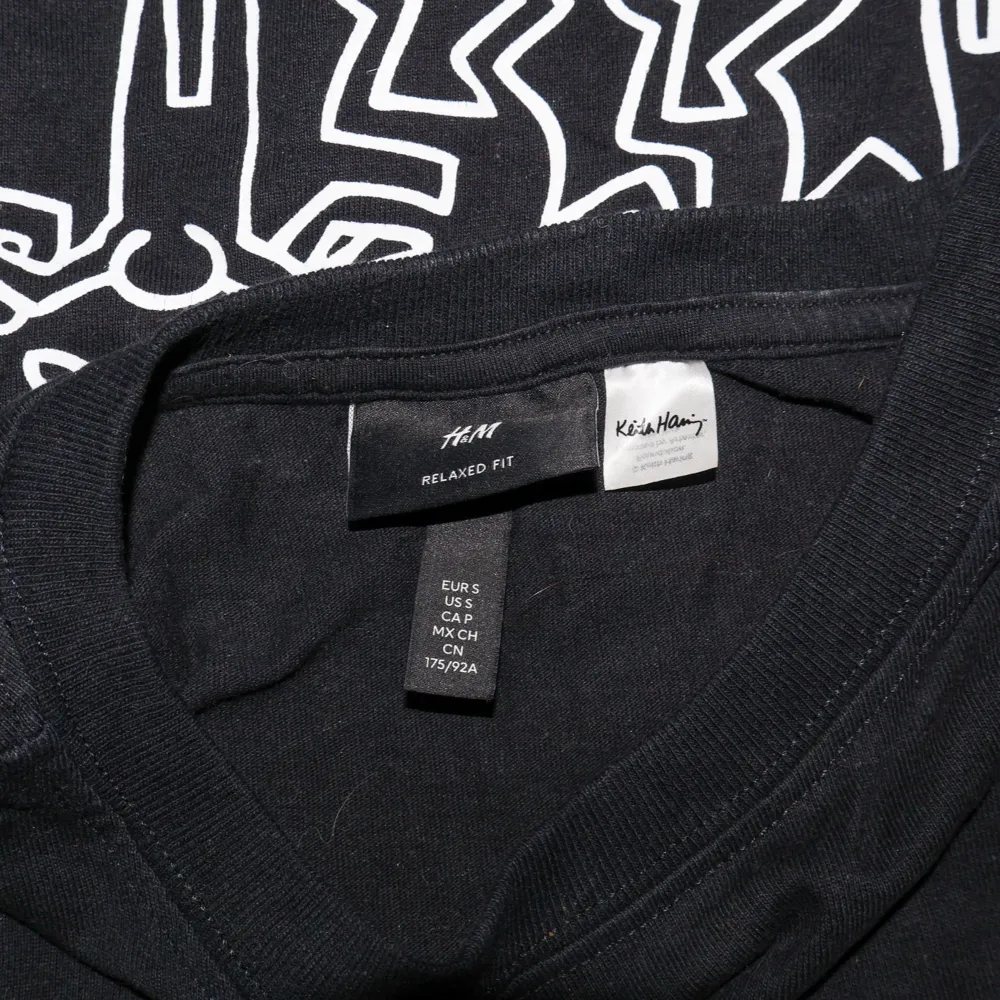 Säljer en marinblå t-shirt från H&M med ett Keith Haring-tryck fram och bak. Den är i bomull och har en relaxed fit, perfekt för en avslappnad stil.. T-paidat.