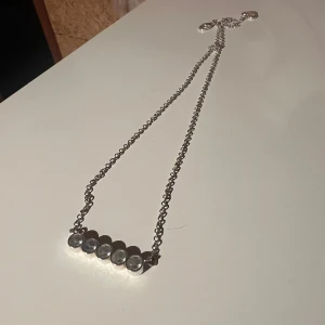 Silverfärgat halsband med stenar - Snyggt silverfärgat halsband med sex klara stenar i rad. Perfekt för att ge en elegant touch till vilken outfit som helst. Kedjan är tunn och justerbar för att passa olika längder. Passar både till vardags och festliga tillfällen.