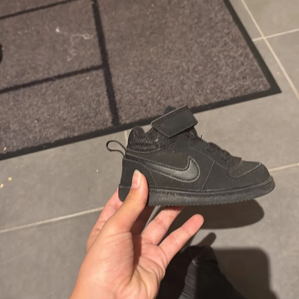 Säljer ett par svarta Nike sneakers för babysar mycket bra skick. Skorna har en stilren design med kardborreband och snörning för enkel på- och avtagning. Perfekta för både lek och vardag!. Skor.