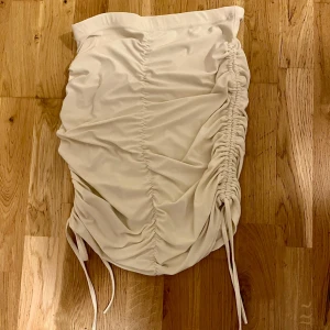 Vit kjol med snörning - Säljer en superfin vit kjol med snörning på sidan som ger en snygg rynkad effekt. Perfekt för sommaren eller en utekväll! Kjolen är i bra skick och har en tight passform som framhäver figuren. Den är gjord i ett mjukt och bekvämt material. Ny