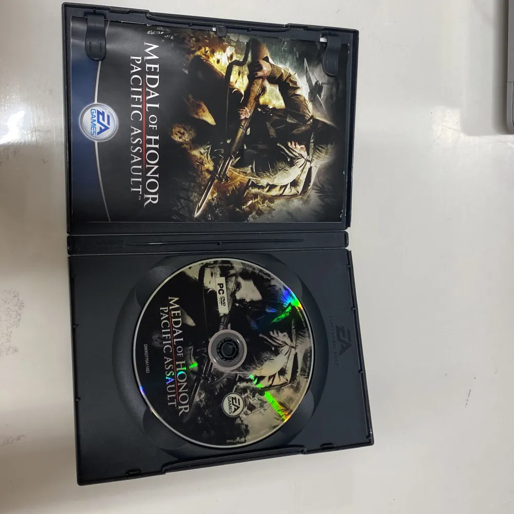 Säljer ett PC-spel, Medal of Honor: Pacific Assault, från EA Games. Spelet är i en svart DVD-fodral med en dramatisk omslagsbild av en soldat i strid. Det är märkt för 16+ och har en svensk flagga på framsidan. Perfekt för dig som gillar actionfyllda krigsspel och vill uppleva intensiva strider i Stilla havet.. Övrigt.