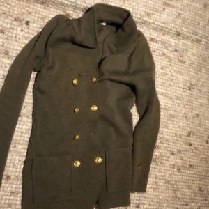 Grön Busnel kappa med guldknappar - Jag säljer den här jättesnygga, ikoniska busnel koftan. Den kostade ungefär 5000 ny men kunde tyvärr inte hitta någon bild som liknade koftan online. Den har lite hål (bild två) men om man är kunnig och vill så går det förmodligen att reparera. En knapp saknas (bild3) men utöver det tycker jag den är jättefin. Jag säljer endast den för detta pris för att den är lite sliten. Koftan är PERFEKT till hösten och vintern och hade egentligen velat ha den själv men tyvärr är den för stor för mig. 💞