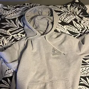 Säljer en grå hoodie från Palace i bra skick. Den har en stor logga på ryggen och en mindre på bröstet. Perfekt för höst och vår, med en skön passform och klassisk stil. Huvan har dragsko och det finns en praktisk magficka framtill. Perfekt för streetwear-stilen!