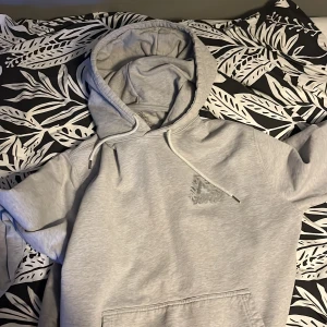 Grå hoodie från Palace - Säljer en grå hoodie från Palace i bra skick. Den har en stor logga på ryggen och en mindre på bröstet. Perfekt för höst och vår, med en skön passform och klassisk stil. Huvan har dragsko och det finns en praktisk magficka framtill. Perfekt för streetwear-stilen!