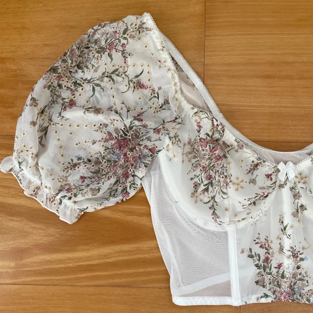 Säljer en superfin blommig offshoulder korsettopp med puffiga ärmar. Den är vit med ett romantiskt blommönster i rosa och grönt. Toppen har en söt liten rosett framtill och är gjord i ett lätt och luftigt material. Perfekt för sommarens fester eller en mysig picknick i parken! Passar nog främst på m-l men funkar även på mig som har xs, sitter lite lösare bara. . Toppar.