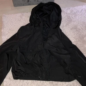 Svart vindjacka från Pull&Bear - Säljer en svart vindjacka från Pull&Bear i storlek XS. Jackan har en praktisk huva och dragkedja framtill. Perfekt för blåsiga dagar och har en cool, avslappnad stil. Använd ett fåtal gånger, så den är i mycket bra skick. Passar perfekt till både vardag och utflykter!