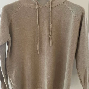 Beige hoodie i bomull - Säljer en stilren beige hoodie i mjukt bomullsmaterial. Perfekt för höst och vår med sin bekväma passform och långa ärmar. Den har en klassisk huva med dragsko och ribbade muddar vid ärmslut och nederkant. Enkelt att matcha med det mesta i garderoben!