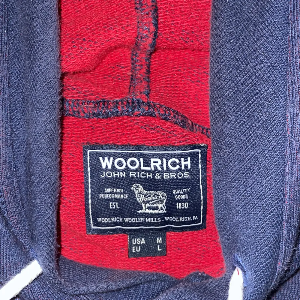 Säljer en snygg mörkblå hoodie från Woolrich med röd text på framsidan. Den har en  ficka fram och en  huva med vita snören. Perfekt för kyliga dagar och passar till det mesta. Använd ett fåtal gånger, så den är i bra skick. . Tröjor & Koftor.