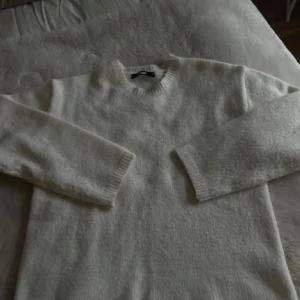 Vit stickad tröja - Mysig vit stickad tröja perfekt för kyliga dagar. Den har en klassisk rund hals och långa ärmar med ribbade muddar. Passar både till vardags och lite finare tillfällen. Superbekväm och stilren!