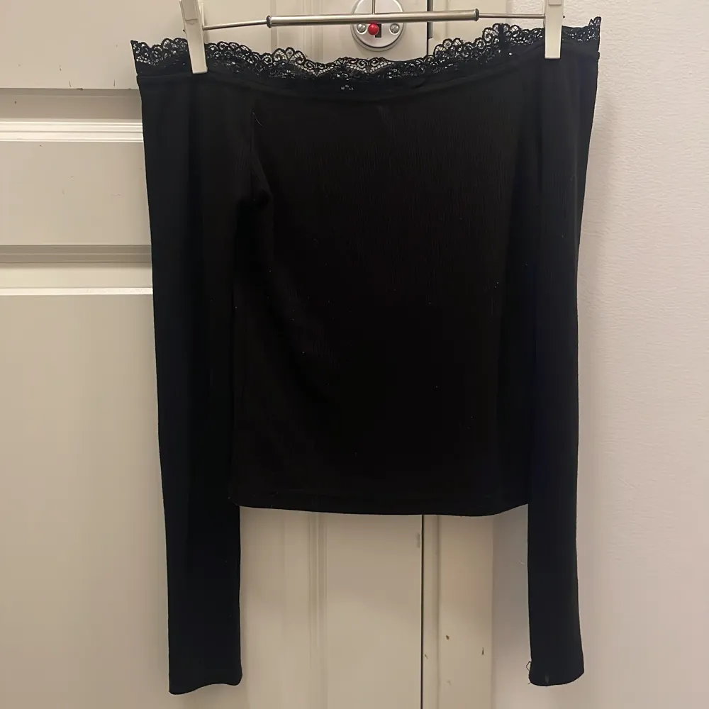 Snygg svart långärmad topp från Bik Bok i storlek XS. Toppen har en offshoulder-design med vacker spetsdetalj vid halsringningen. Perfekt för både vardag och festliga tillfällen. 🖤. Toppar.