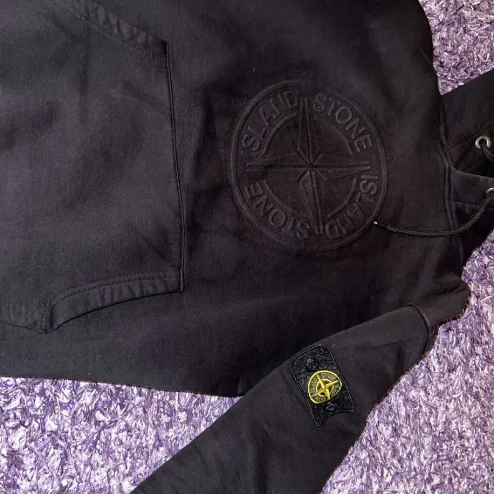 Säljer en svart hoodie från Stone Island i bra skick. Den har en stor ficka fram och det ikoniska Stone Island-märket på ärmen. Perfekt för höst och vinter, och passar både till vardags och chill. Grymt snygg och bekväm!. Tröjor & Koftor.