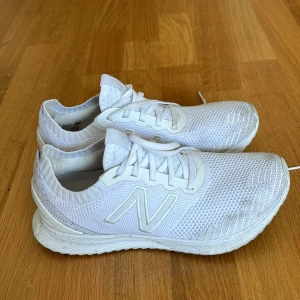 Vita sneakers från New Balance - Säljer ett par vita sneakers från New Balance i storlek 40,5. Skorna är i bra skick och har en snygg och stilren design med snörning. Perfekta för både träning och vardagsbruk. De är gjorda i ett lätt och andningsbart material som gör dem bekväma.