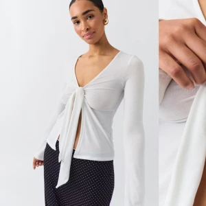 Vit långärmad topp med knyt - Säljer en superfin vit långärmad topp med knyt framtill. Den har en v-ringad design och är perfekt för både vardag och fest. Materialet är mjukt och bekvämt, vilket gör den till ett måste i garderoben!